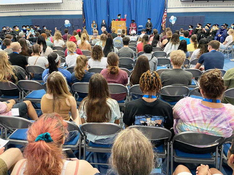 Students seated in gym listening to speaker at podium 